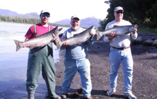 Three men on shore holding salmon