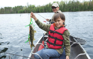 boy in a fishing boat holding a small bass