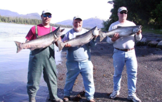 Three men on shore holding large salmon