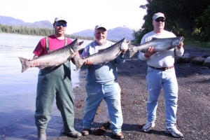 A trio of anglers hold up their catches while salmon fishing in Alaska.
